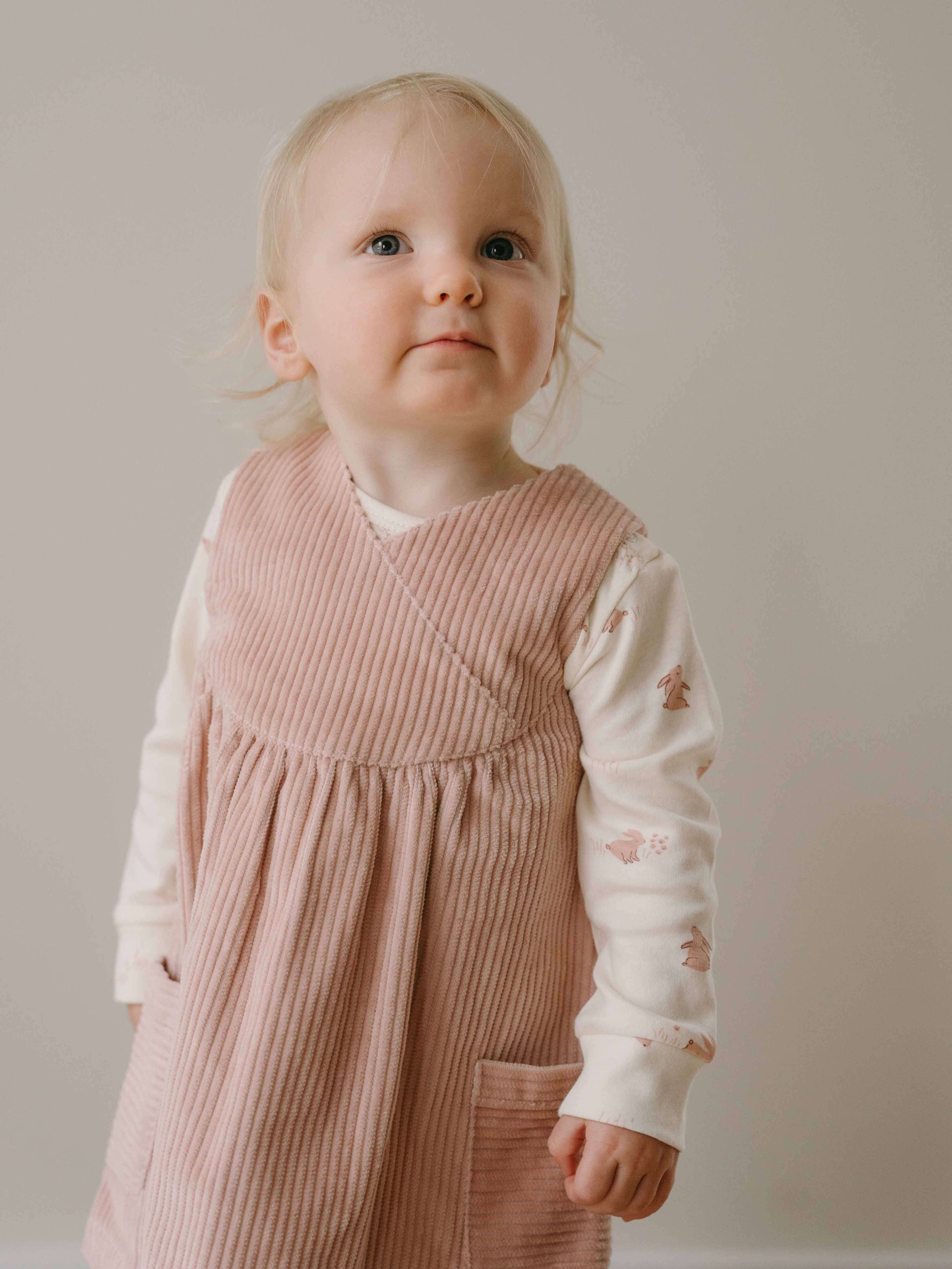 Young child wearing a pink dress over a white shirt with floral patterns against a plain background