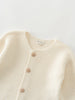 Close-up of a cream-colored knitted cotton cardigan with button details on a light gray background