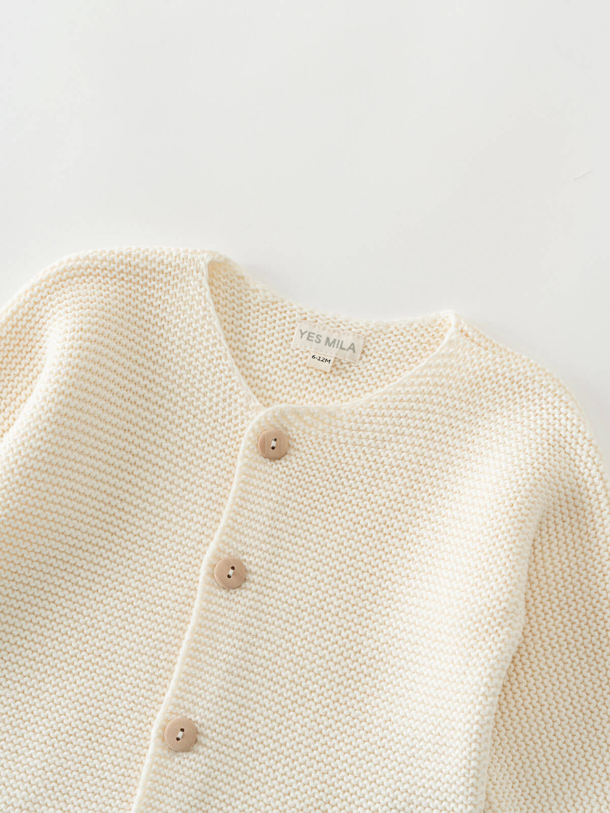 Close-up of a cream-colored knitted cotton cardigan with button details on a light gray background