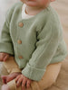 Child wearing a green knitted cardigan with brown buttons on a neutral background