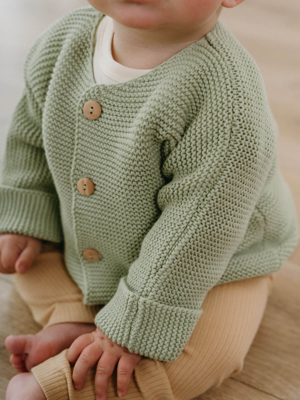 Child wearing a green knitted cardigan with brown buttons on a neutral background