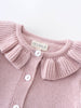 Pink knitted cardigan with ruffled collar and 'YES MILA' label on a light gray background