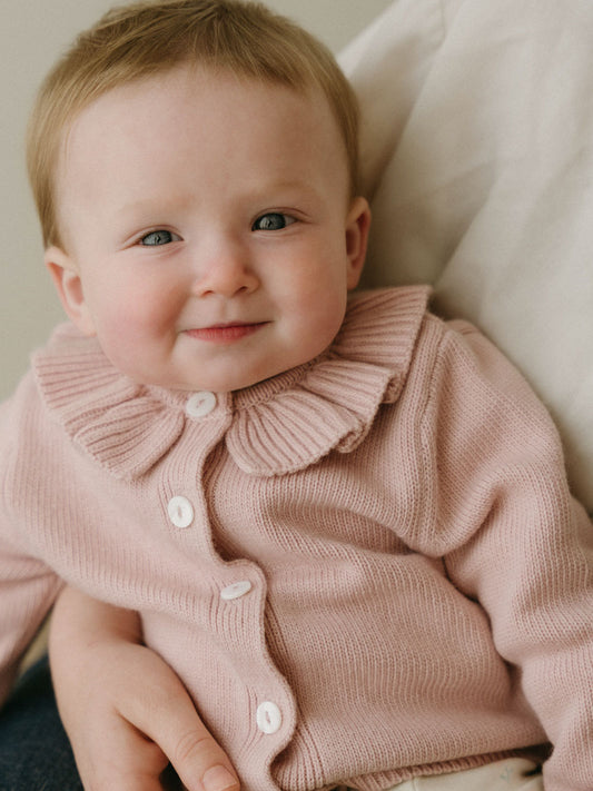 Baby wearing a pink knit cardigan with ruffle collar and white buttons Baby Ruffle Cardigan - Blush Baby girl