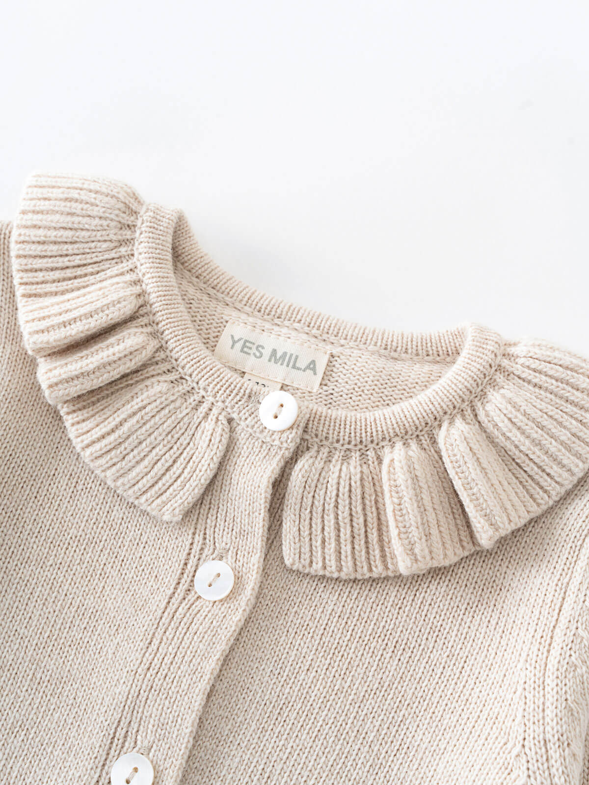 Beige knitted cardigan with ruffled collar and visible brand label on a light background Baby Ruffle Cardigan - Ecru Baby girl