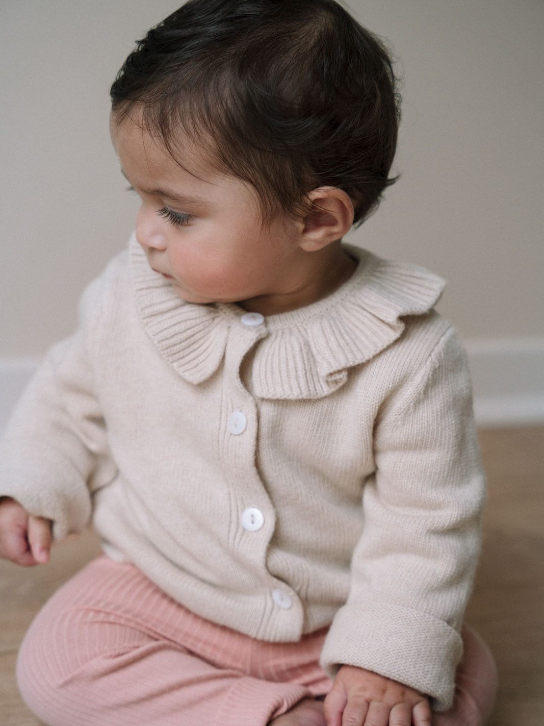 Young child in cream knit cardigan with ruffle collar and pink pants Baby Ruffle Cardigan - Ecru Baby girl