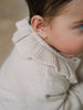 Close-up of a child wearing a cream ribbed knit turtleneck sweater Baby Ruffle Cardigan - Ecru Baby girl
