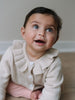Baby wearing cream knit cardigan with ruffle collar and white buttons Baby Ruffle Cardigan - Ecru Baby girl