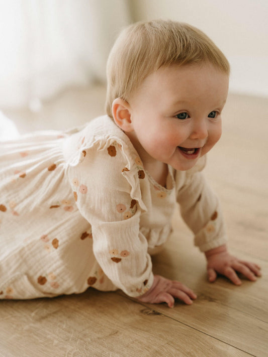 Baby in a white dress with floral patterns on a wooden floor