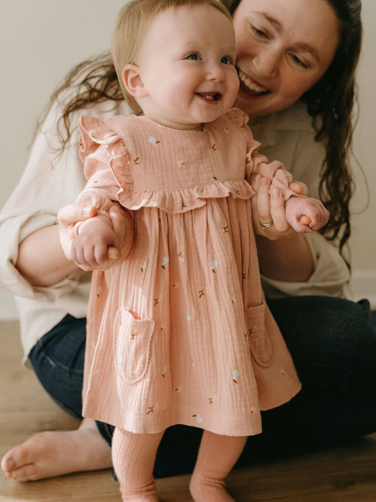 Woman holding a baby wearing a pink dress with ruffled sleeves and a pocket. Baby Woven Dress - Autumn Harvest Rosehip Baby girl