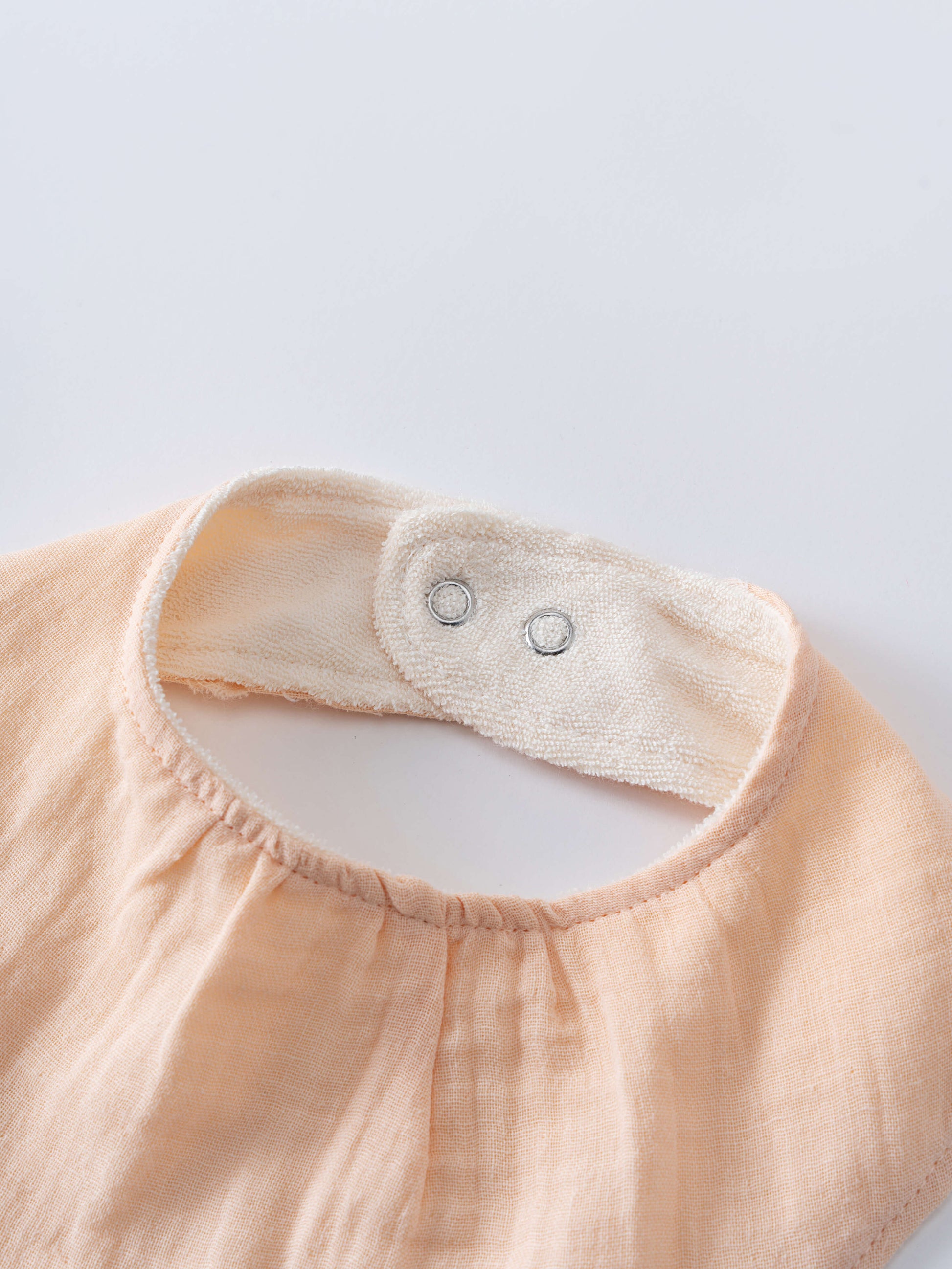 Close-up of a peach-colored garment with a collar on a light gray background Bandana Bibs 3 Pack - Petal Paws Baby girl