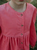 Close-up of a pink dress with buttons on a blurred natural background