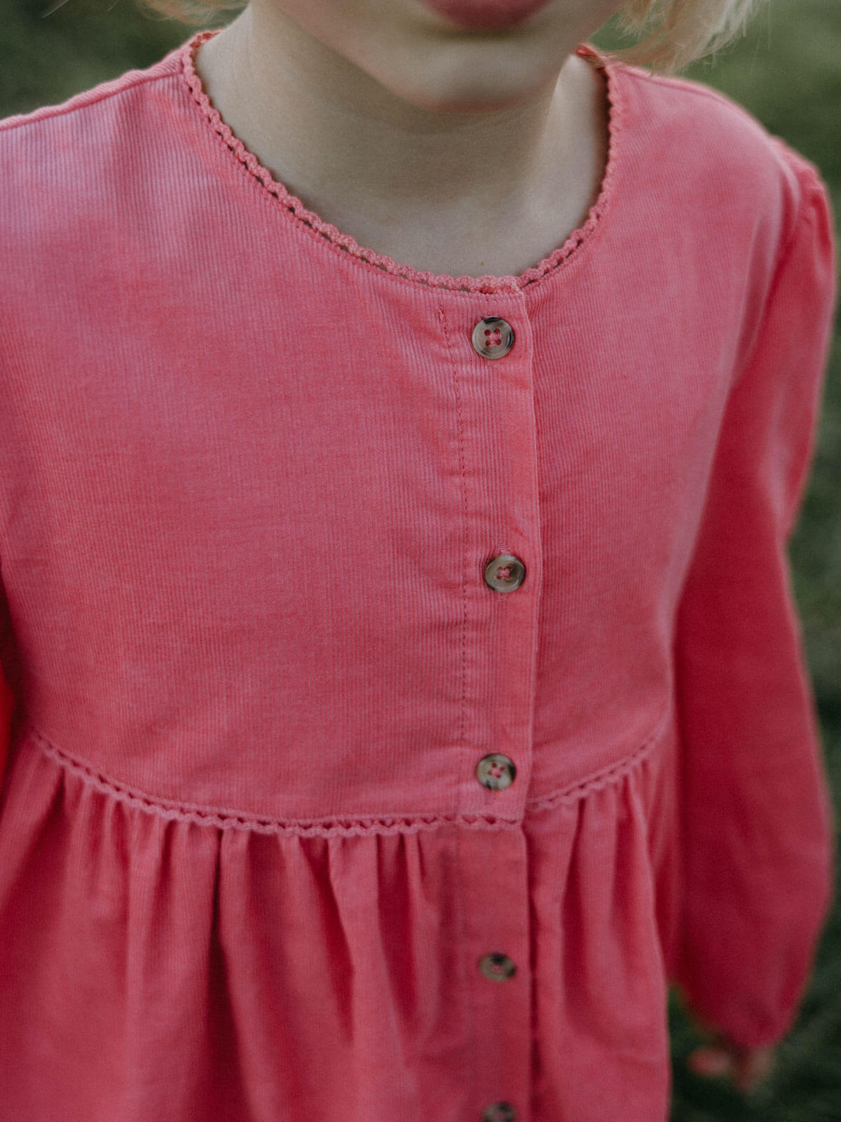 Close-up of a pink dress with buttons on a blurred natural background