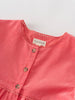 Close-up of a coral pink dress with 'YES MILA' label on a light gray background
