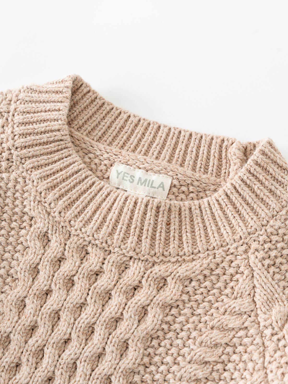 Close-up of a beige knitted sweater with 'YES MILA' label on a white background Cable Knit Jumper - Wicker Boys