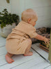 Child in a beige outfit playing with a toy on a white wooden floor.