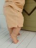 Child wearing a beige towel around their waist on a wooden floor.
