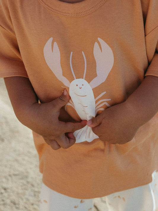 Child wearing a shirt with a lobster design, holding a small white lobster toy.