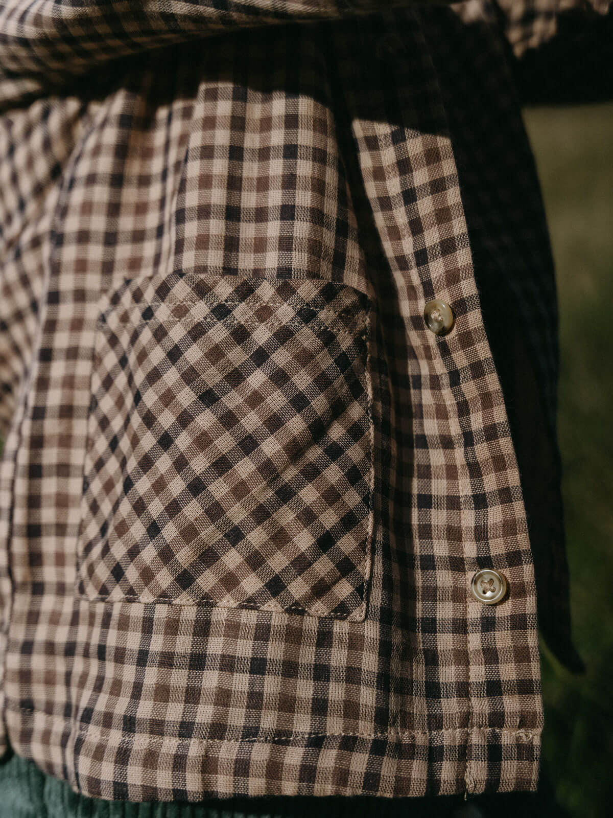 Close-up of a brown and black checkered jacket with a pocket.