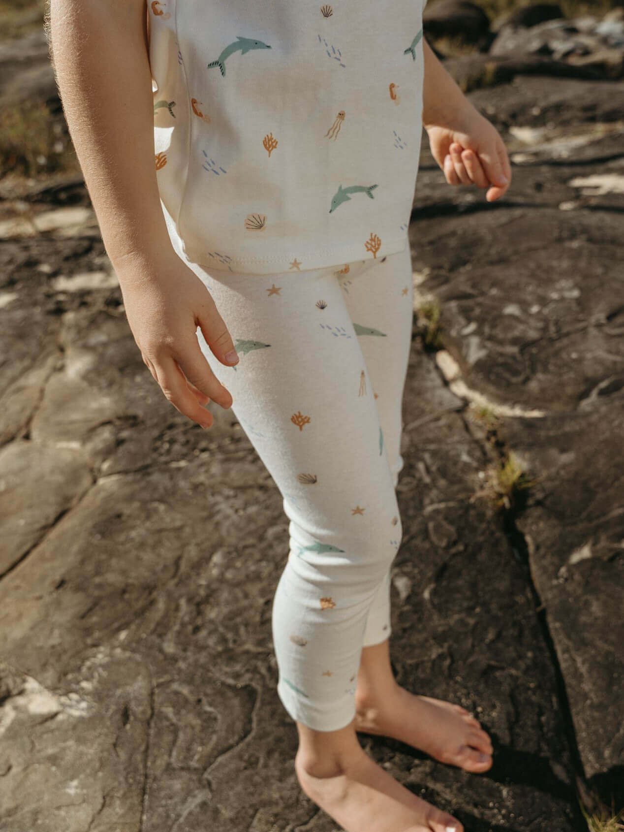 Child wearing a patterned outfit standing on a rocky surface