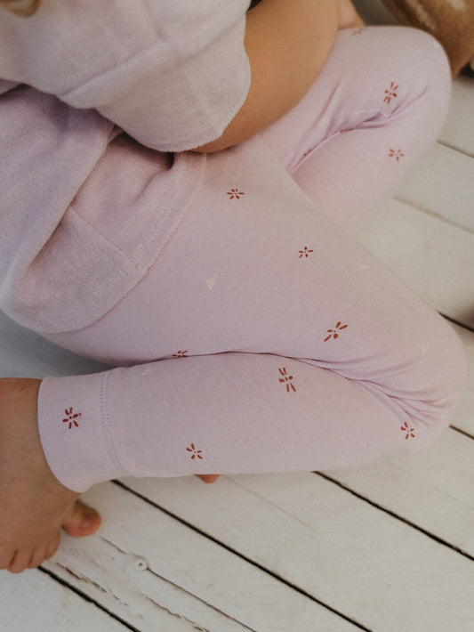 Close-up of a child's legs wearing light purple leggings with floral patterns on a wooden floor.
