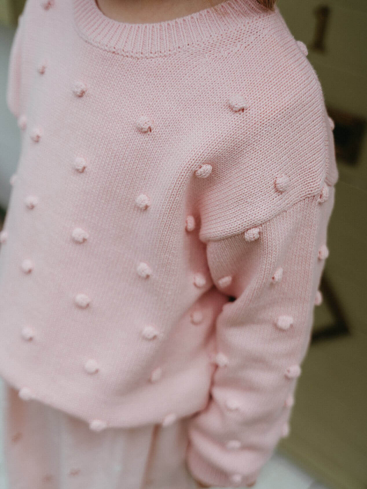 Pink knitted sweater with pom-pom details on a blurred background