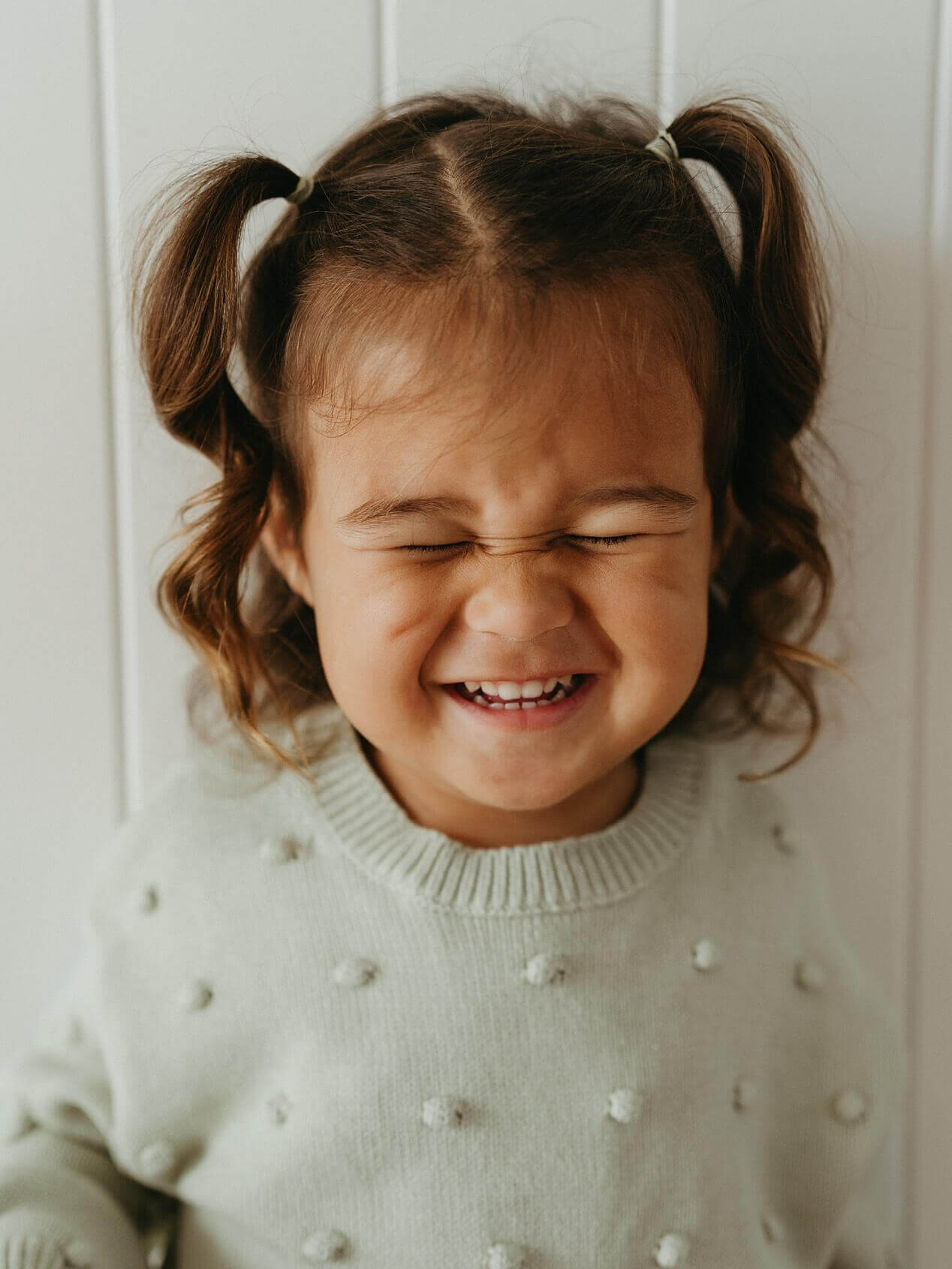Child with pigtails wearing a light green sweater with white polka dots, smiling.
