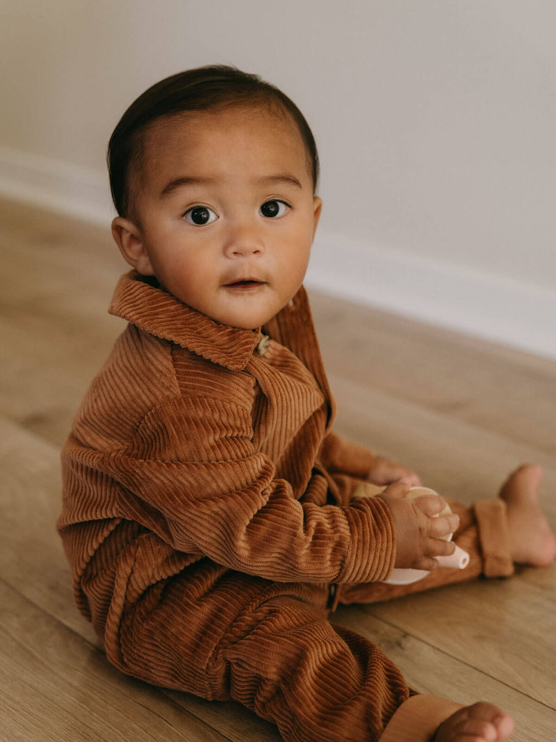 Baby wearing a brown corduroy outfit sitting on a wooden floor. Corduroy Jumpsuit - Russet Baby boy