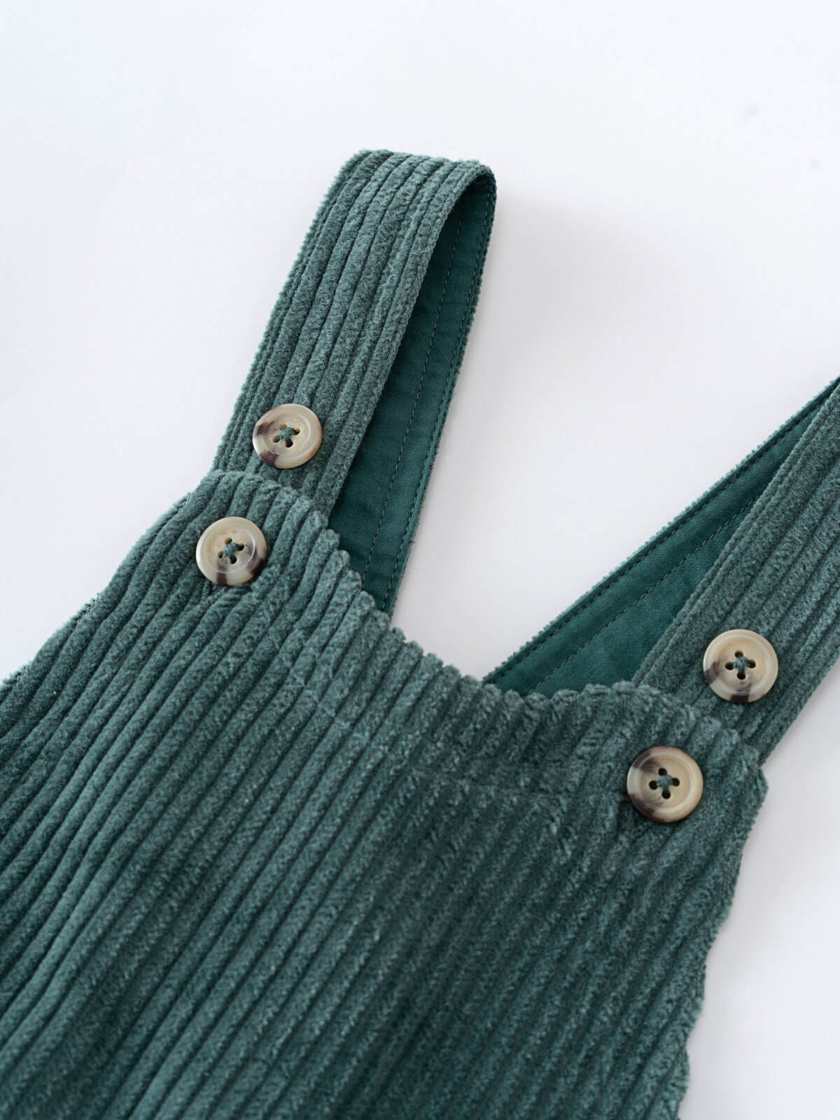 Green corduroy overalls with button details on a white background