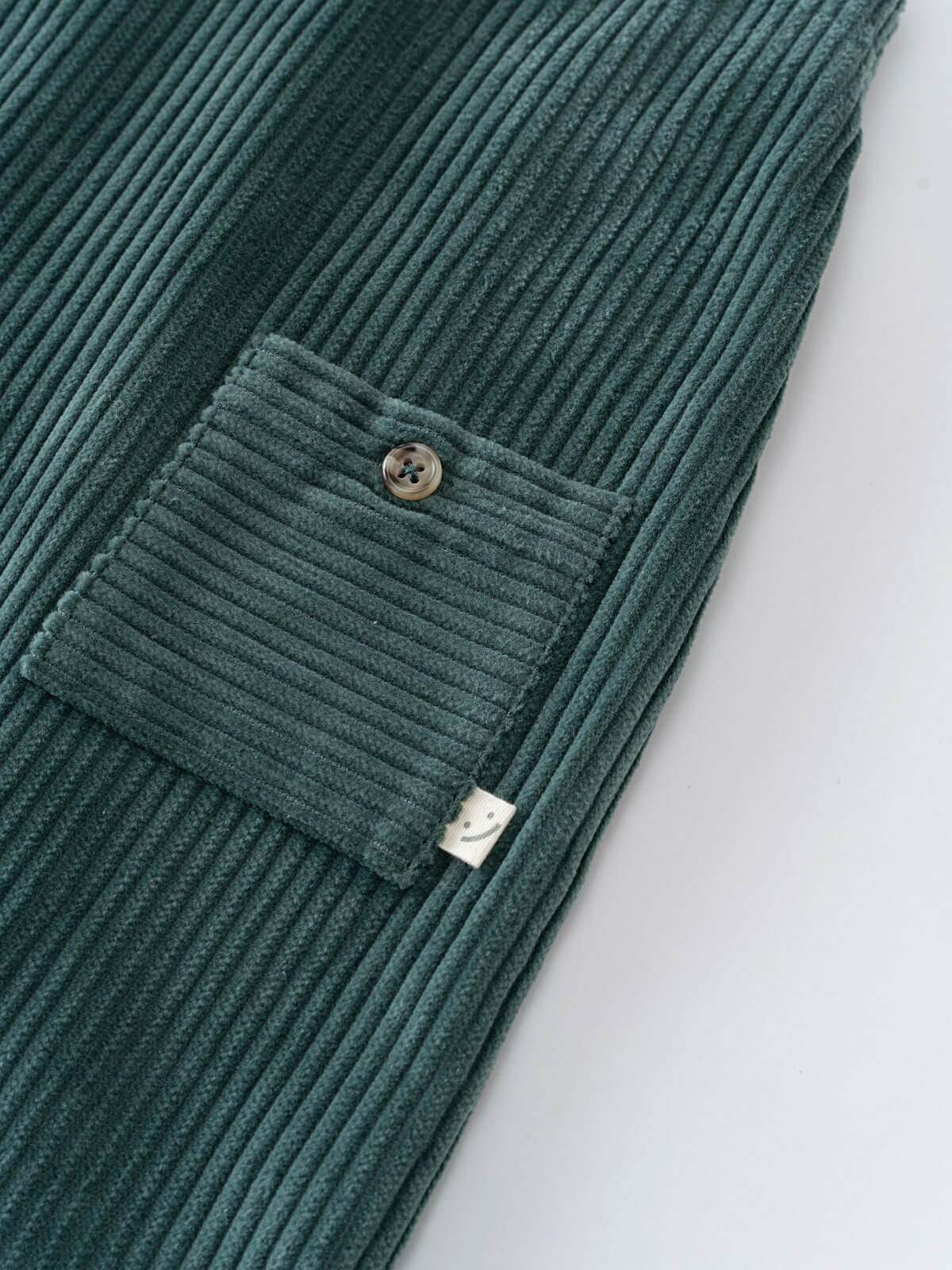 Green corduroy overalls  with a pocket on a light gray background