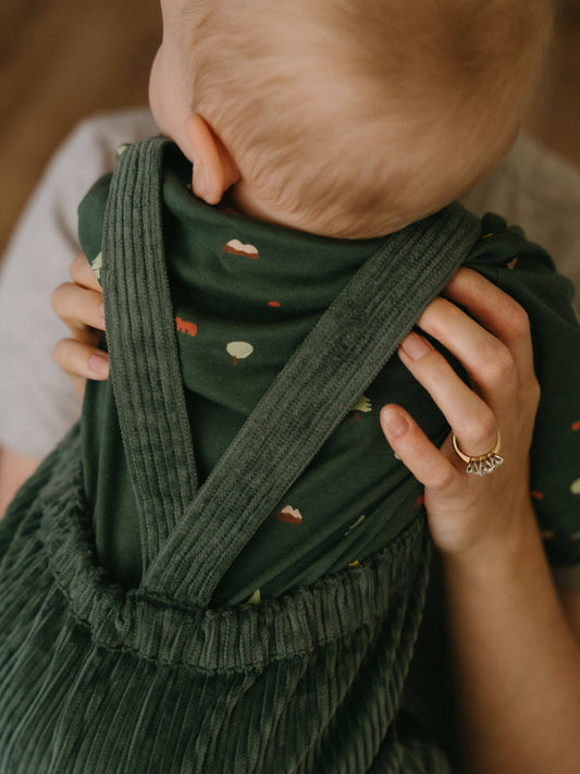 Person holding a baby wrapped in a green wrap with a blurred background