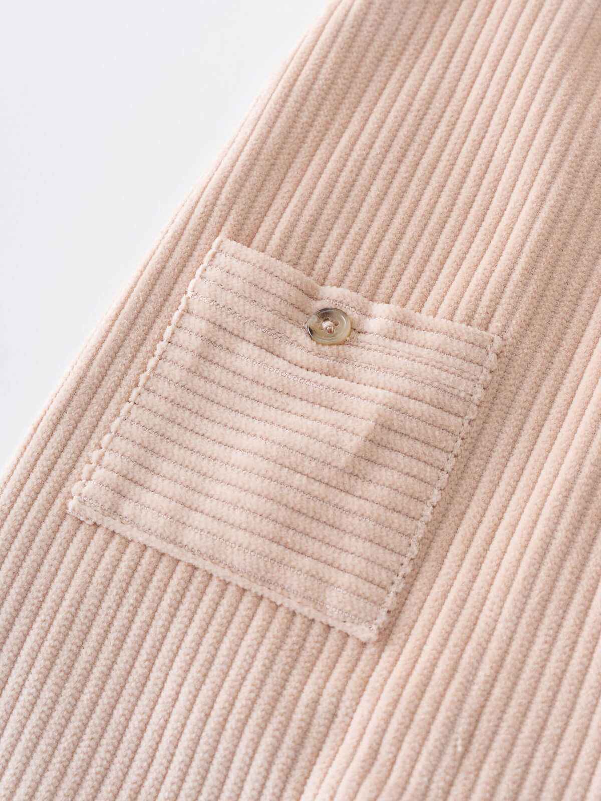 Close-up of a beige corduroy overalls with a pocket on a light gray background