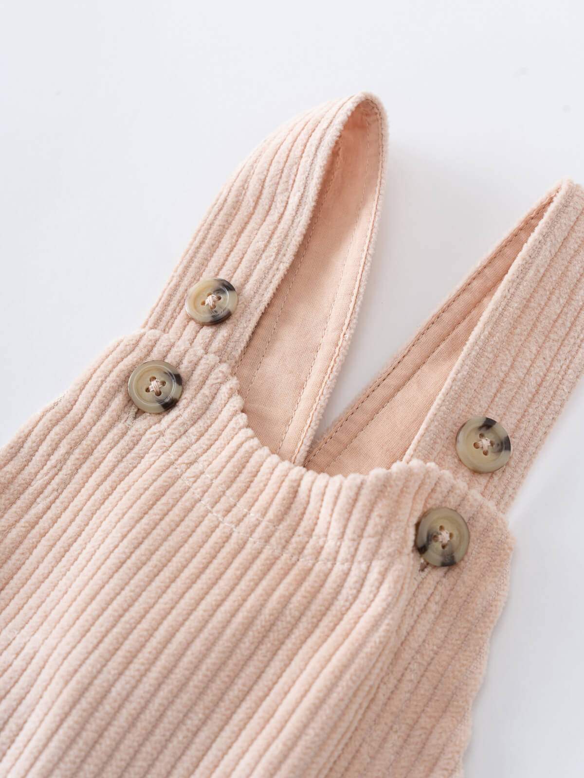 Close-up of a Beige corduroy overalls with button details on a light gray background