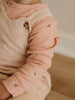 Close-up of a child's outfit with a pink long-sleeve shirt and beige ribbed sweater.