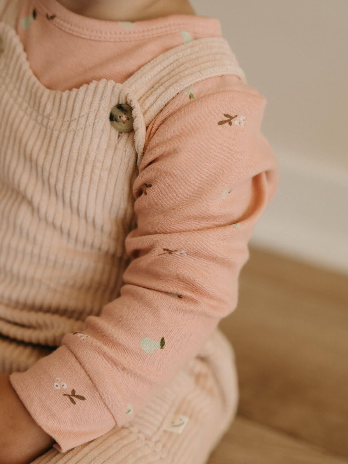Close-up of a child's outfit with a pink long-sleeve shirt and beige ribbed sweater.