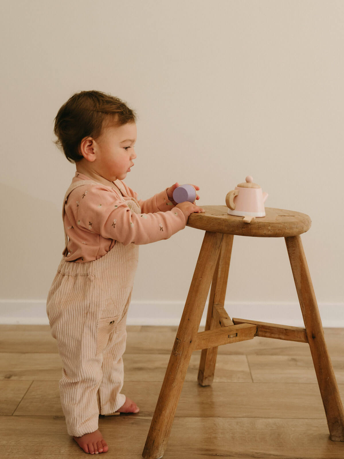 Child playing with toys on a wooden stool against a plain wall.