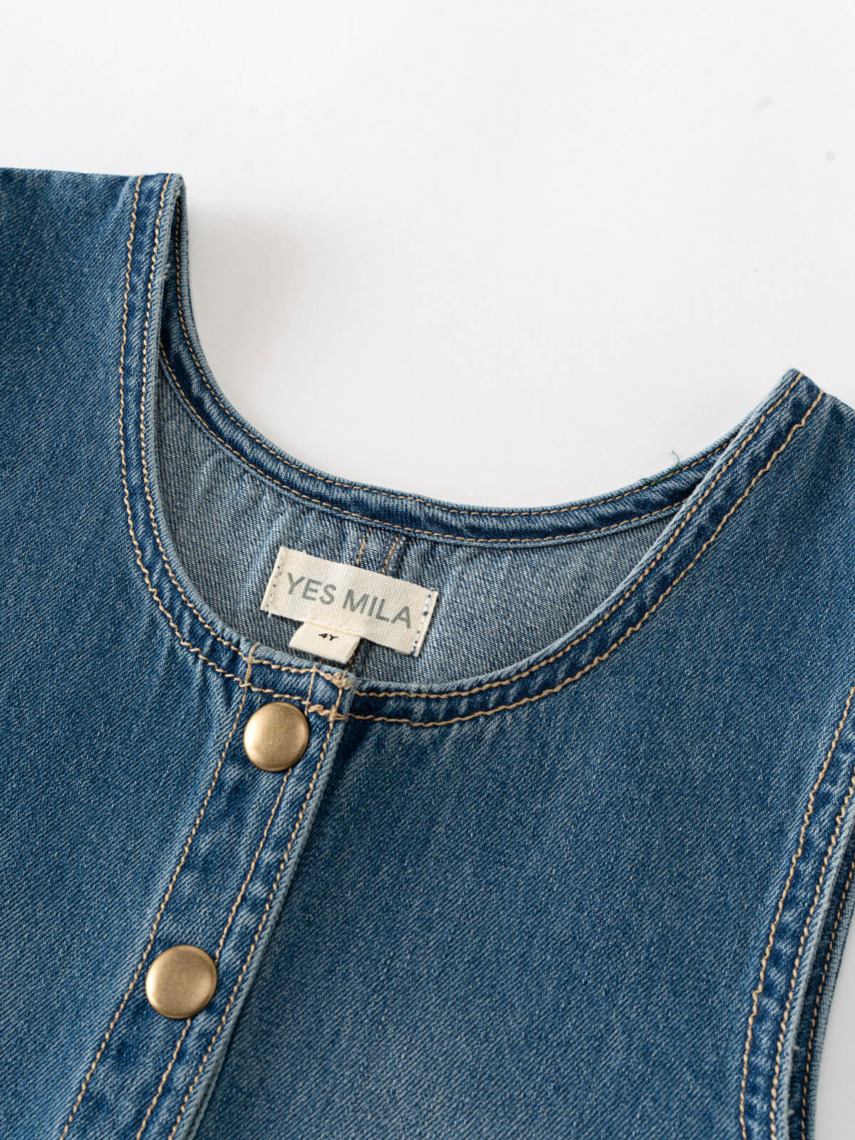 Close-up of a blue denim garment with 'YES MILA' label on a white background Denim Pinafore Dress - Blue Denim Girls