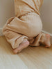 Close-up of a child's legs wearing beige pants on a wooden floor.