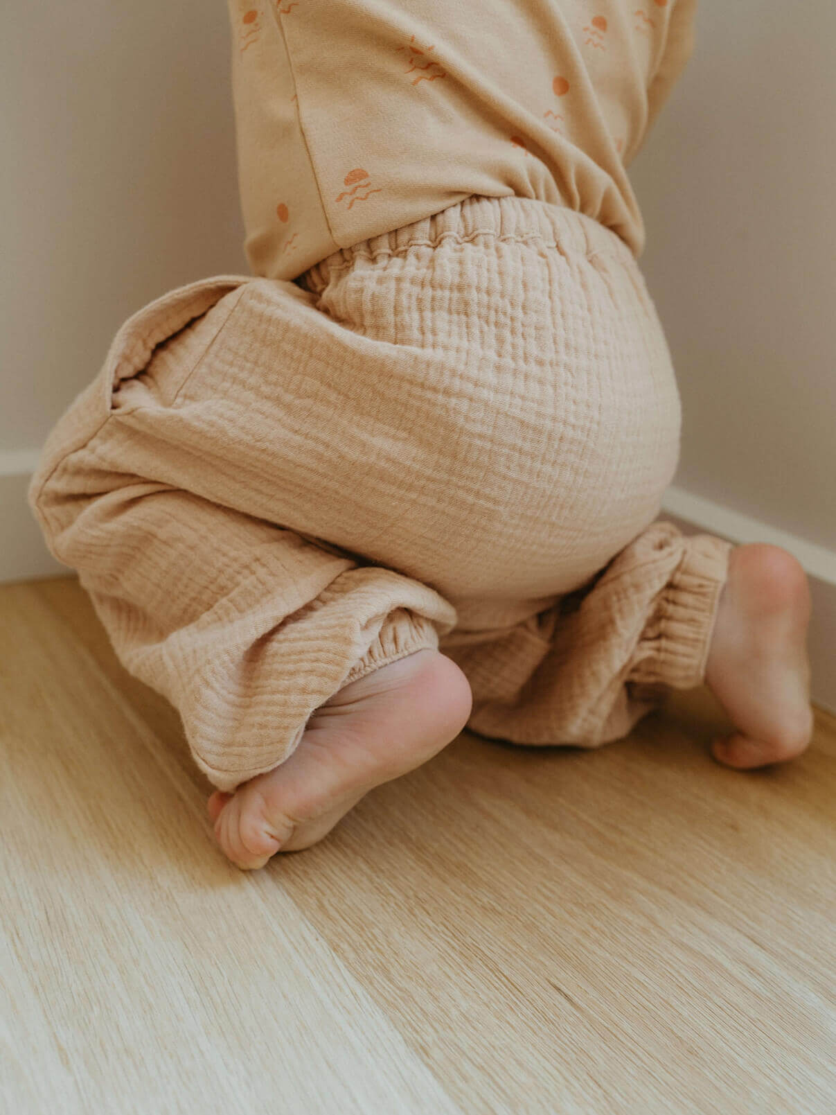 Close-up of a child's legs wearing beige pants on a wooden floor.