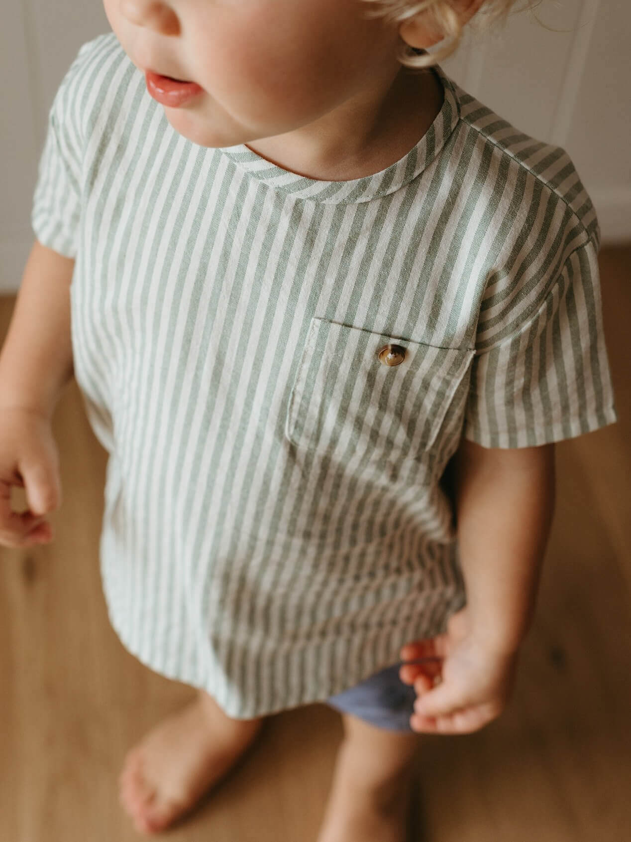 Child wearing a striped shirt with a pocket on a neutral background
