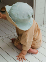 Child wearing a light blue bucket hat and beige outfit on a white wooden floor.
