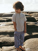 Child wearing a striped shirt and light pants standing on rocks with a natural background