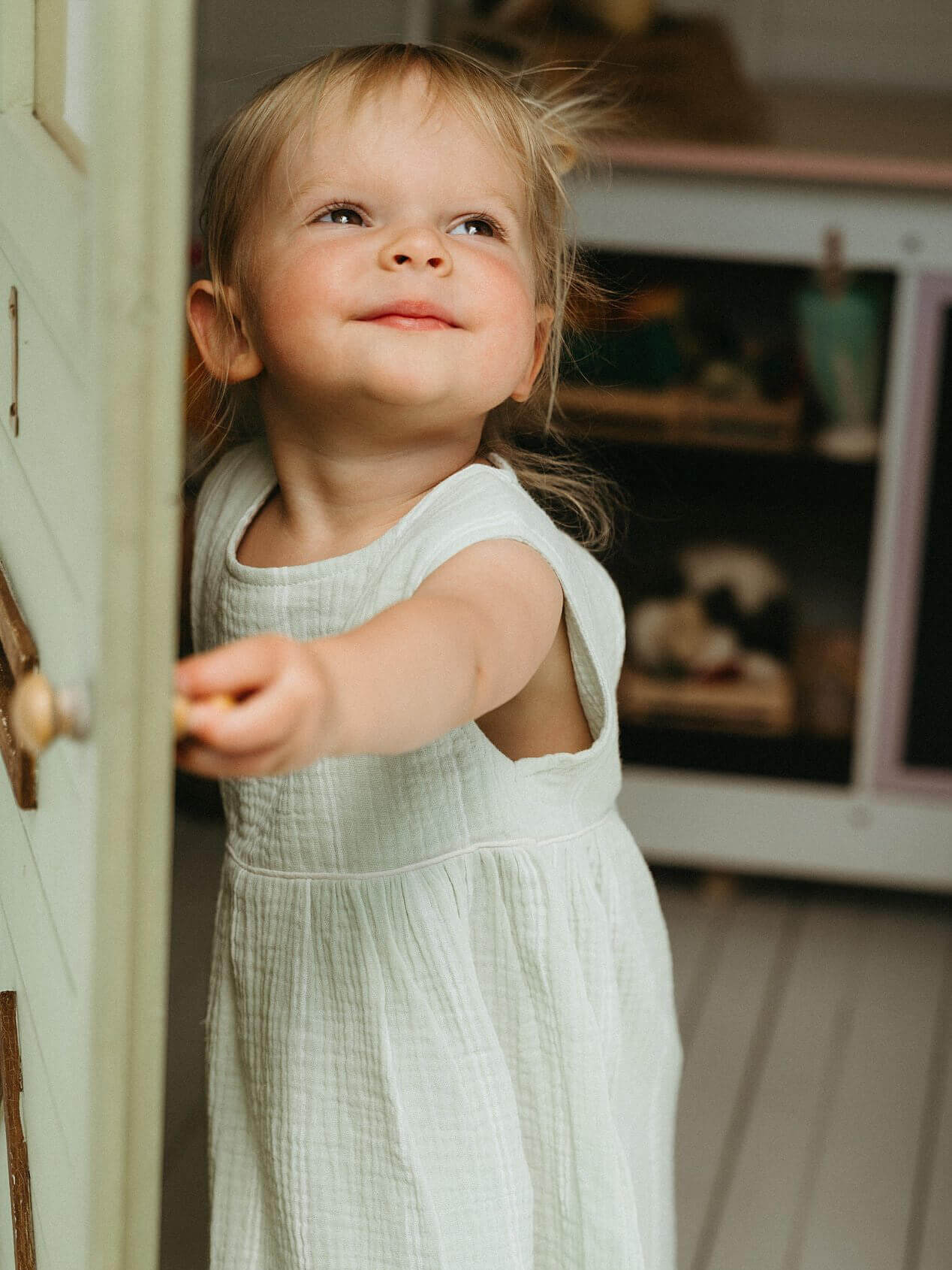 Child in a light green dress peeking out from behind a door