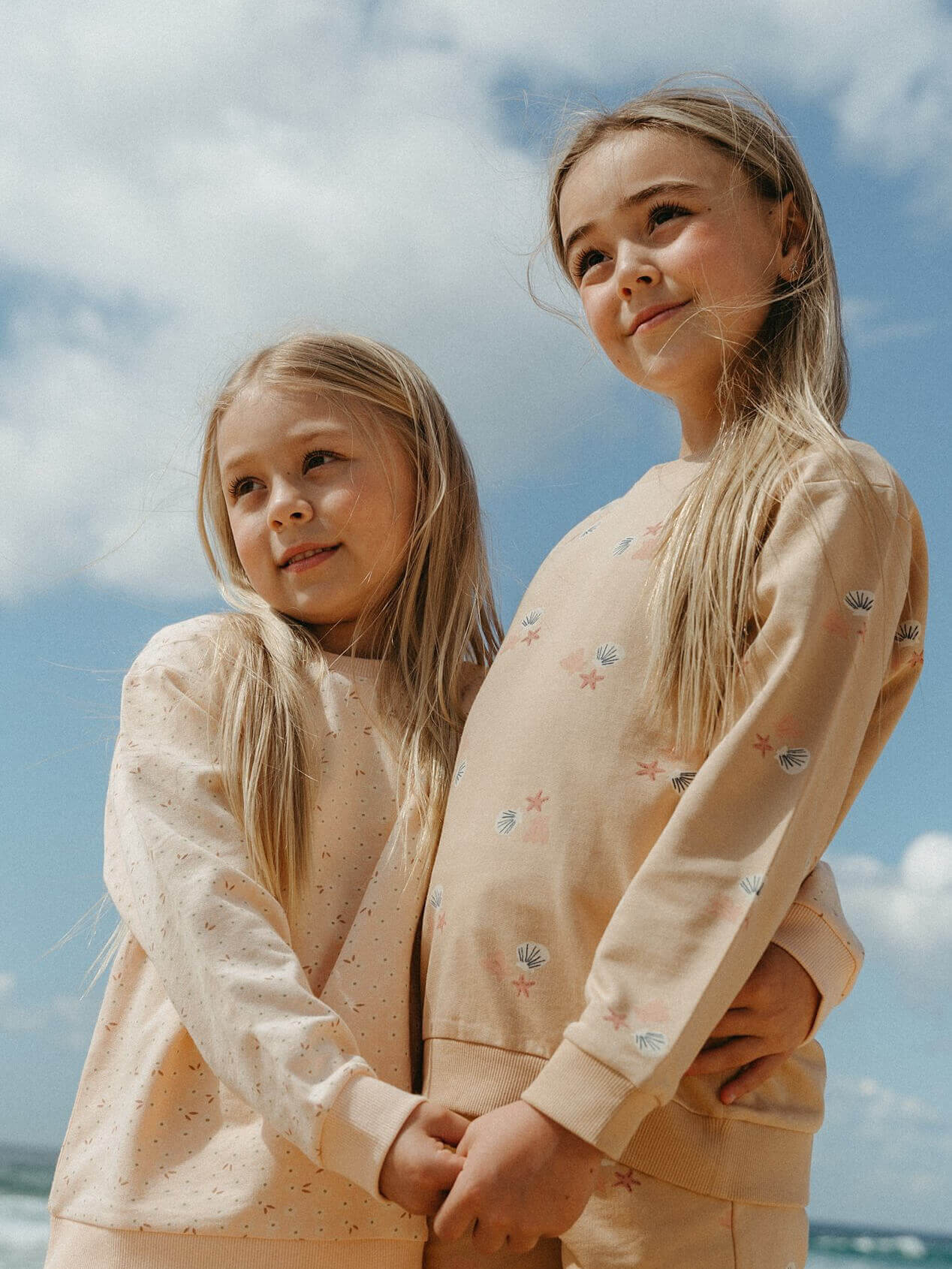 Two young girls wearing matching outfits against a blue sky.