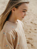 Girl wearing a beige sweater with shell patterns on a blurred beach background
