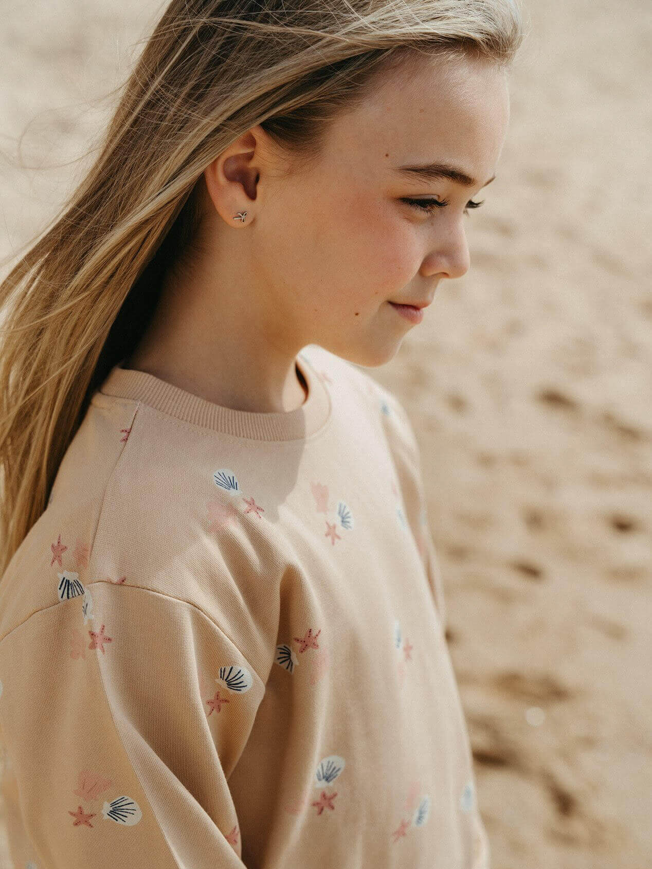 Girl wearing a beige sweater with shell patterns on a blurred beach background
