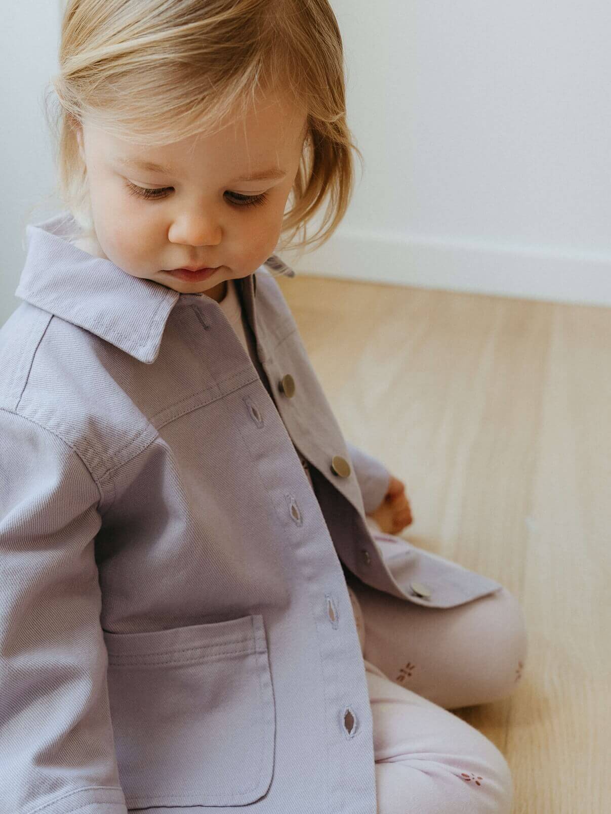 Child wearing a light gray coat sitting on a beige couch.