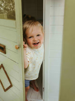 Child peeking out from a playhouse door with a smile