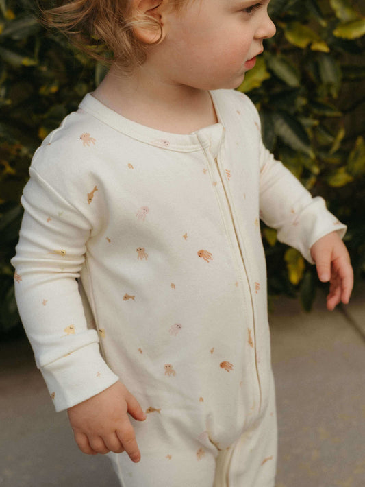 Child wearing a light-colored onesie with subtle patterns outdoors.