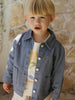 Child wearing a denim jacket in front of a stone wall