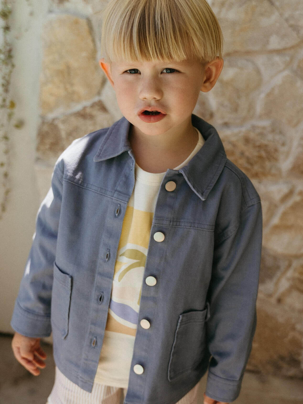 Child wearing a denim jacket in front of a stone wall